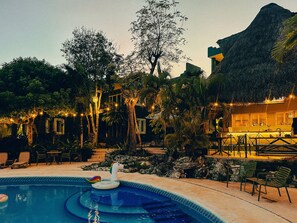 A swimming pool with a unicorn float, surrounded by lounge chairs and a bar area. - Viajero Bacalar Hostel (Bacalar)