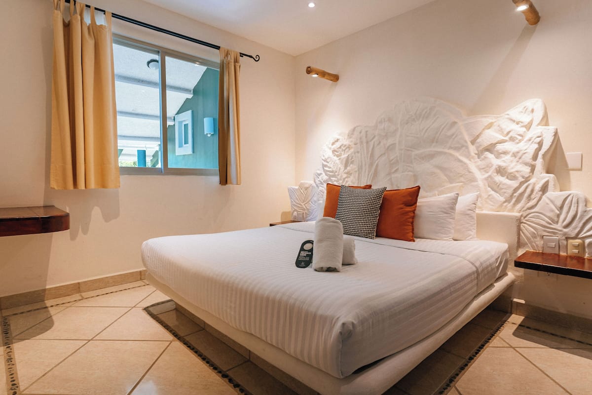 Een hotelkamer met een groot bed, een nachtkastje, gordijnen en een decoratief hoofdeinde.