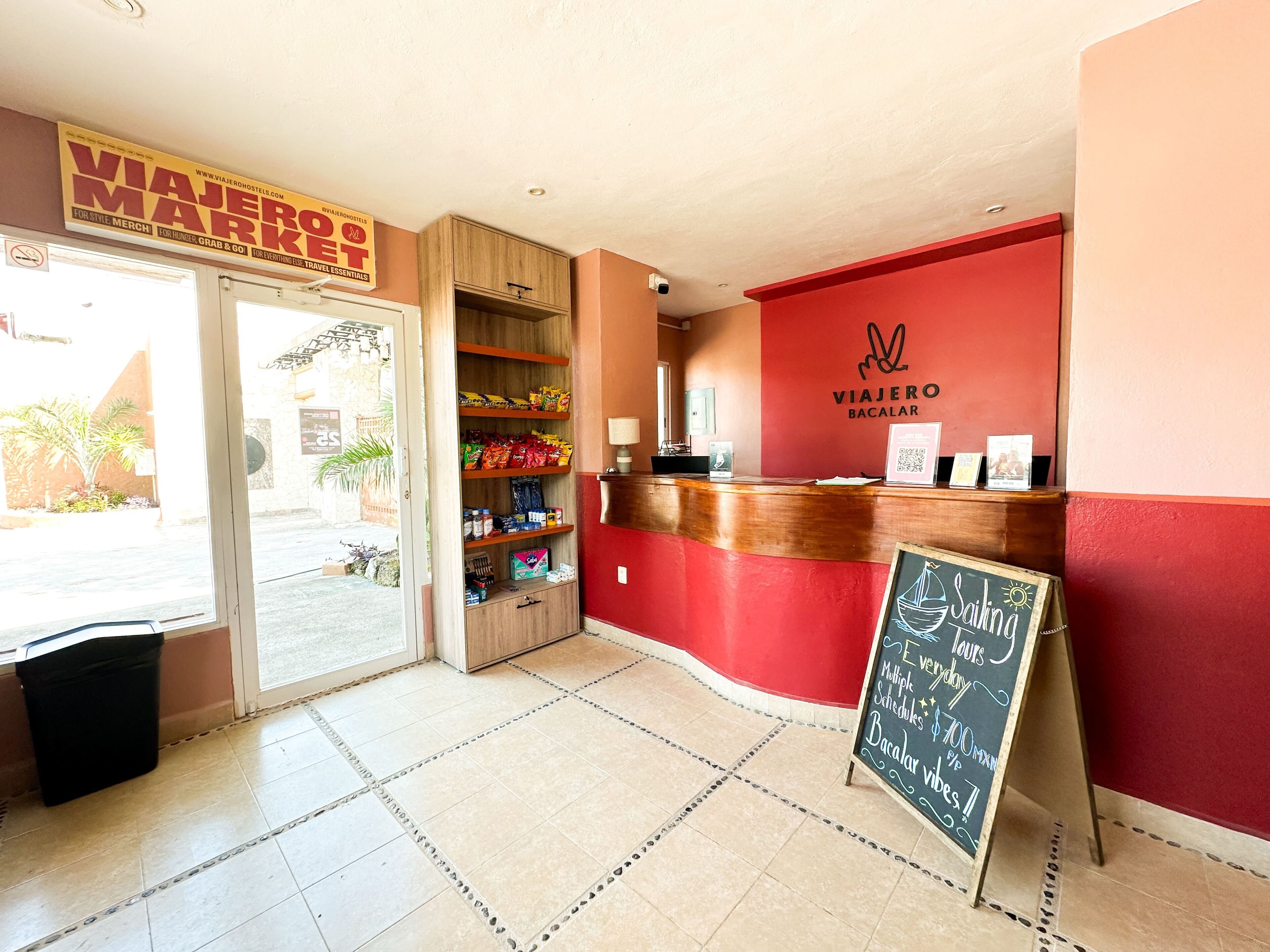 Una zona de recepción con pared roja, mostrador de madera y un cartel que dice 'Viajero Bacalar'.