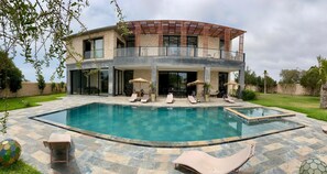 Una casa de dos plantas con piscina, mobiliario de exterior y una pérgola.