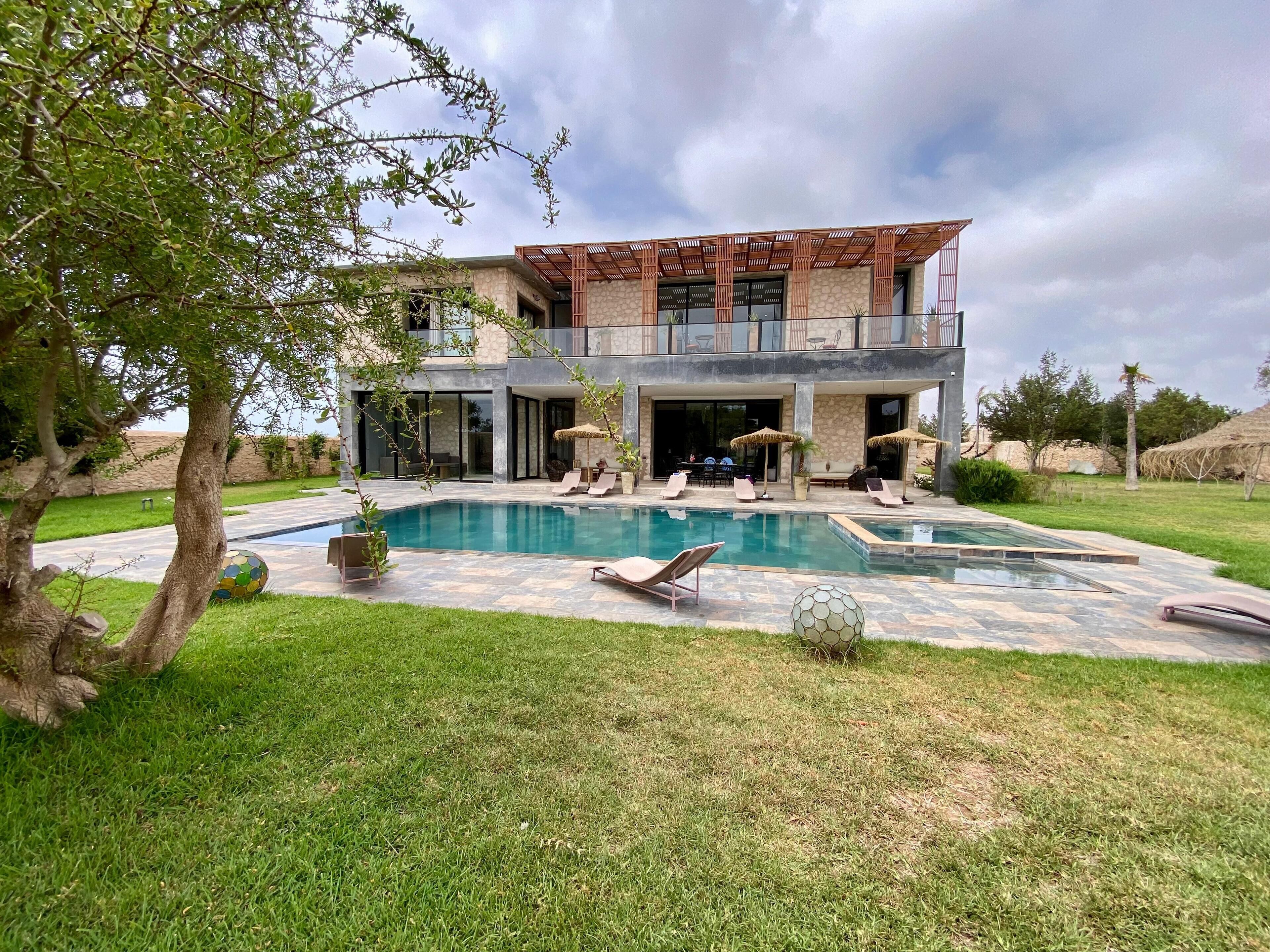 A two-story house with a swimming pool, outdoor seating, and a stone facade.