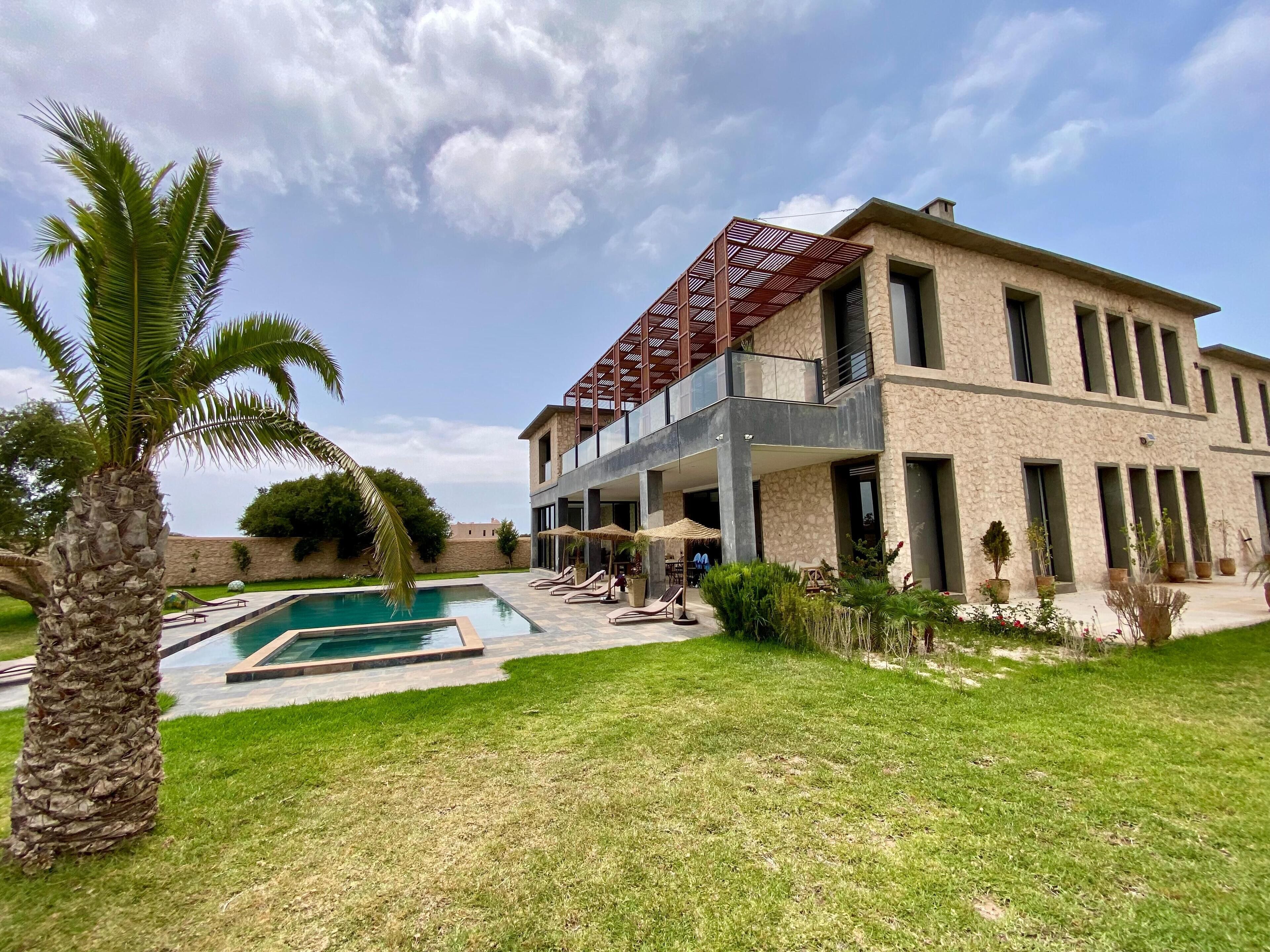 A modern two-story house with a pool, outdoor seating, and a stone facade.