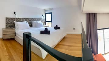 Una habitación de hotel moderna con una cama grande, suelo de madera, una mesita de noche, un escritorio y vistas al exterior.