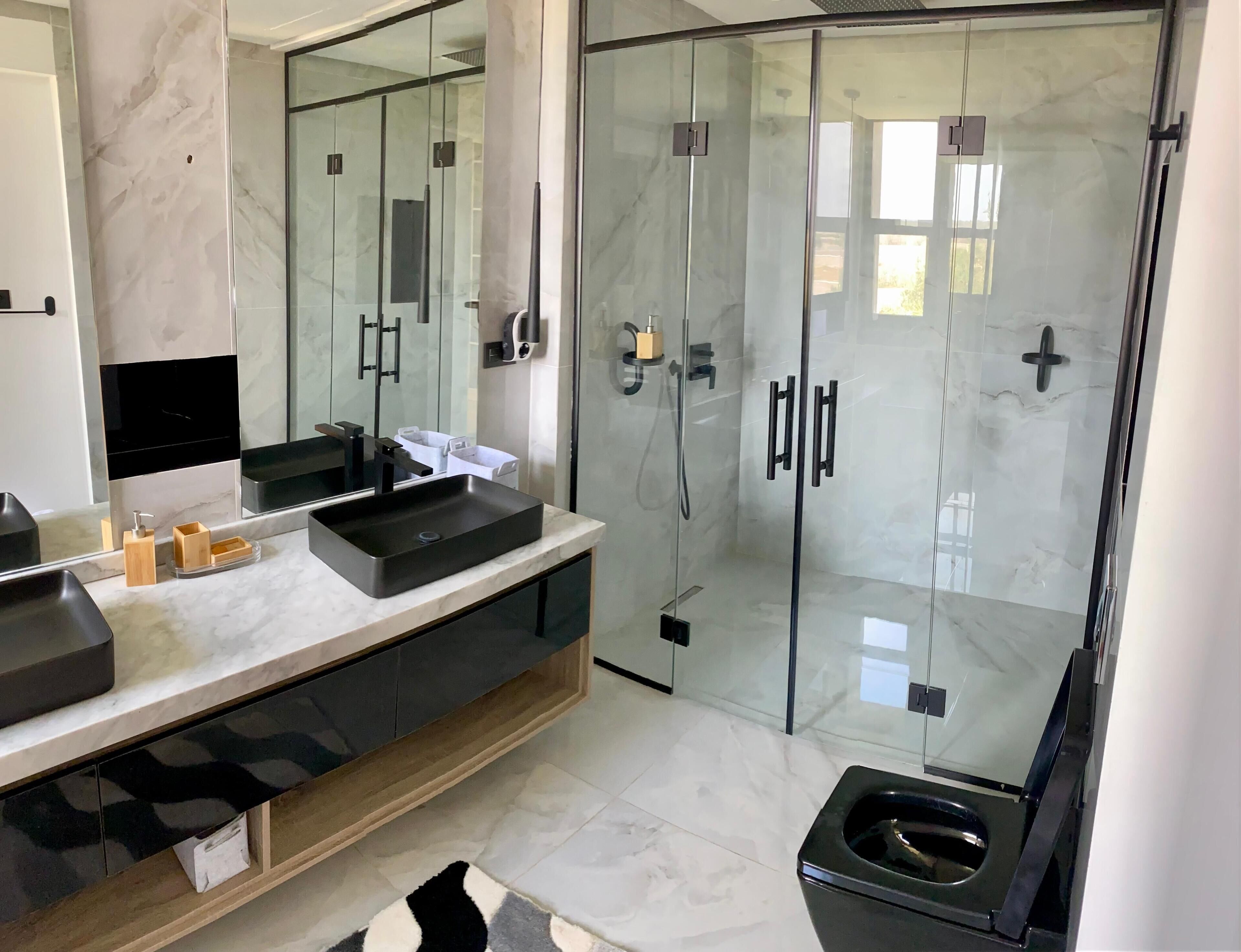 Ein modernes Badezimmer mit einer Glaskabine zur Dusche, einem schwarzen Waschbecken und einer Marmorarbeitsplatte.