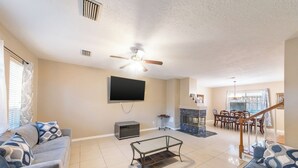 A spacious living room with a ceiling fan, a flat-screen TV, a fireplace, and a staircase leading to another level. - Pet-friendly 3BR Near First Colony Mall (Houston)