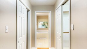A hallway with wooden flooring leading to a bathroom with a bathtub and a window with blinds. - Pet-friendly 3BR Near First Colony Mall (Houston)