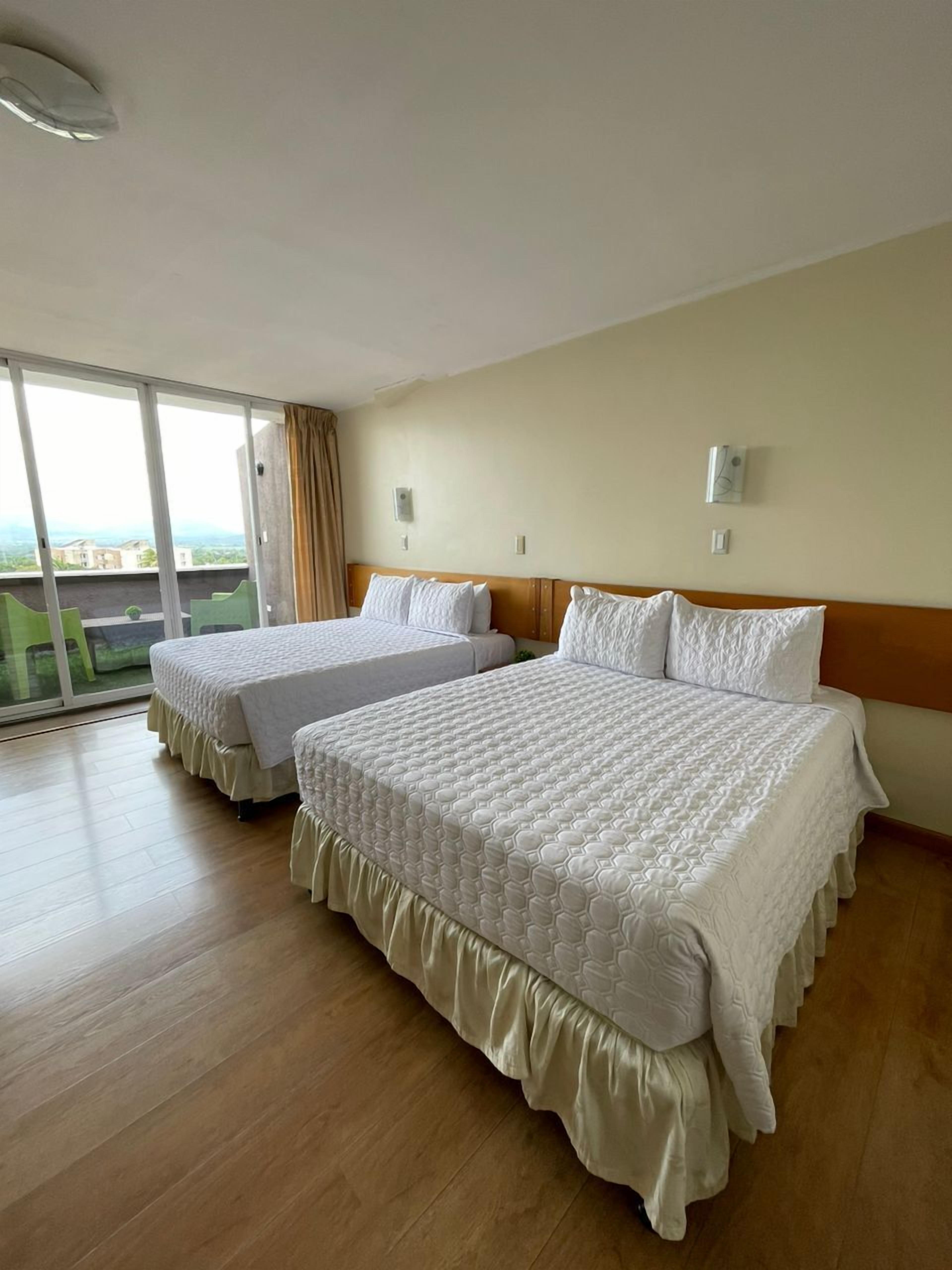 Una habitación de hotel con dos camas, un ventanal con vistas y una puerta corredera al balcón.