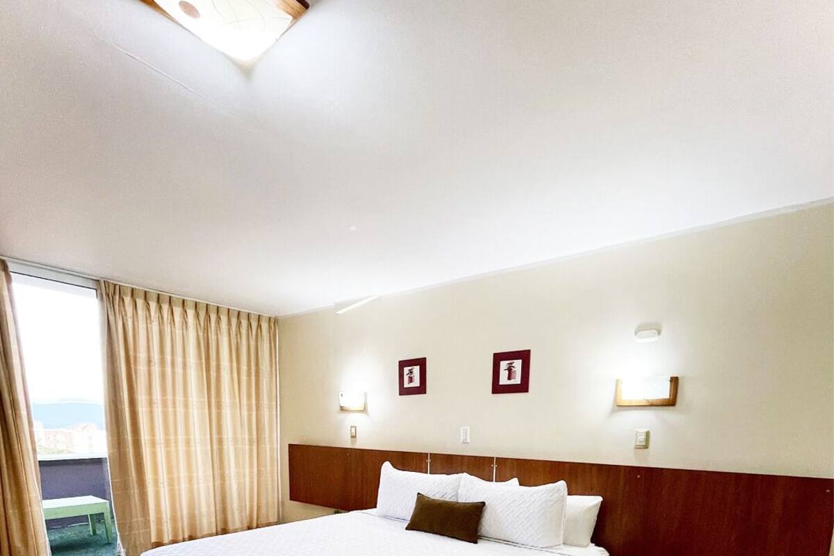 Ein Hotelzimmer mit einem großen Bett, Holzboden und Blick ins Freie durch ein Fenster mit Vorhängen.