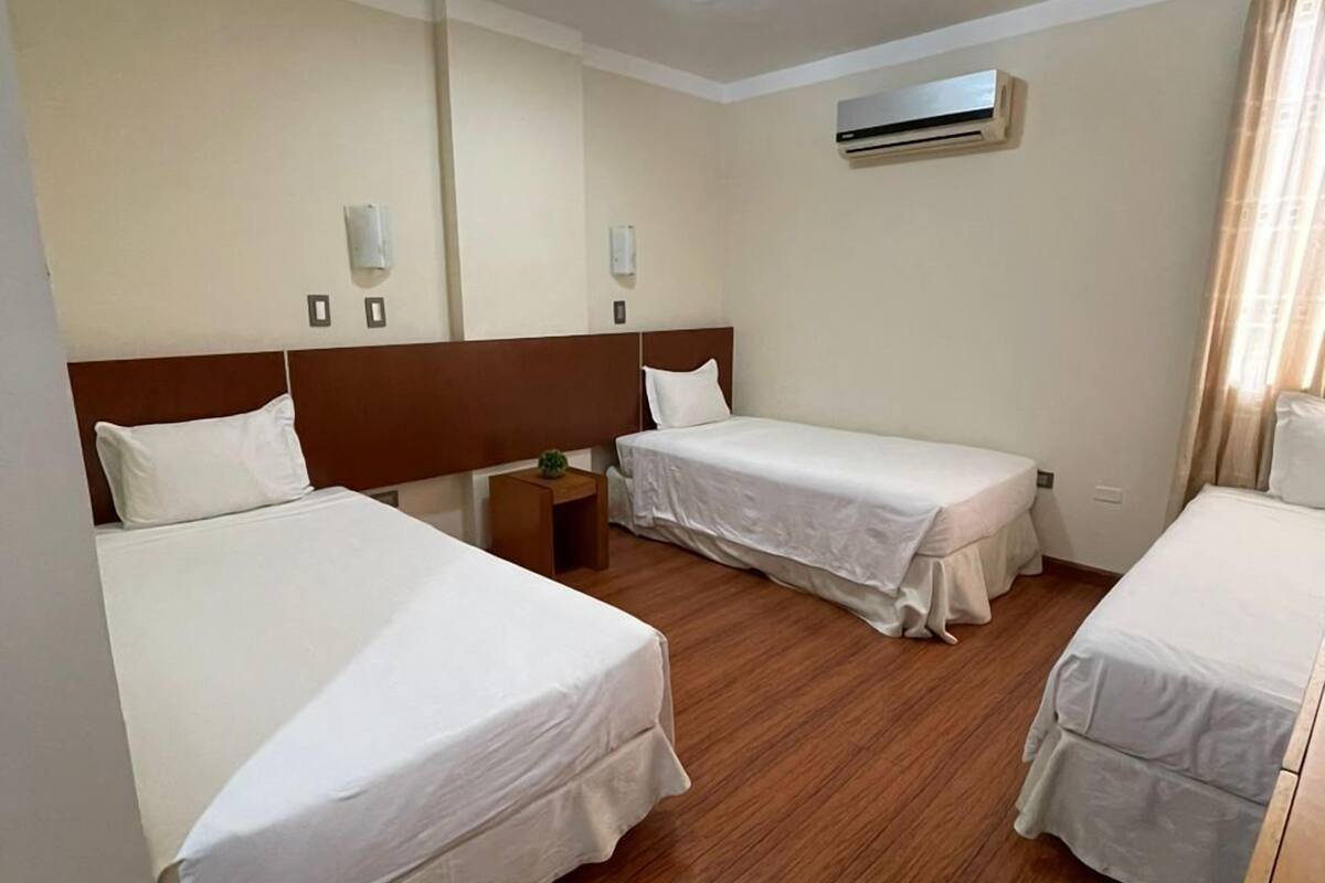 Ein Hotelzimmer mit zwei Einzelbetten, Holzboden, Klimaanlage und einem Nachttisch mit Lampe.