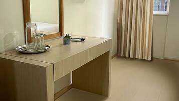 Een hotelkamer met een houten bureau, een flatscreen televisie, een spiegel en een raam met gordijnen.