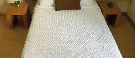 A neatly made bed with a white quilt and a brown pillow, flanked by two nightstands with small green plants.