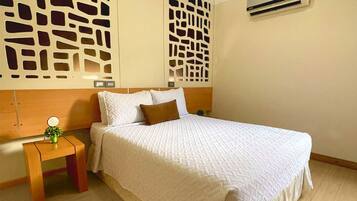 A neatly arranged bedroom with a large bed, a bedside table with a plant, and a wall-mounted air conditioner.