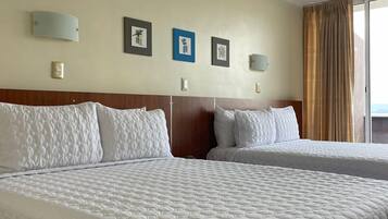Ein Hotelzimmer mit zwei großen Betten, einem Holzkopfstück, einer Wandleuchte und gerahmten Bildern.
