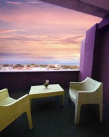 Un balcón con dos sillas de mimbre y una mesa pequeña, con vistas a un paisaje urbano al atardecer.