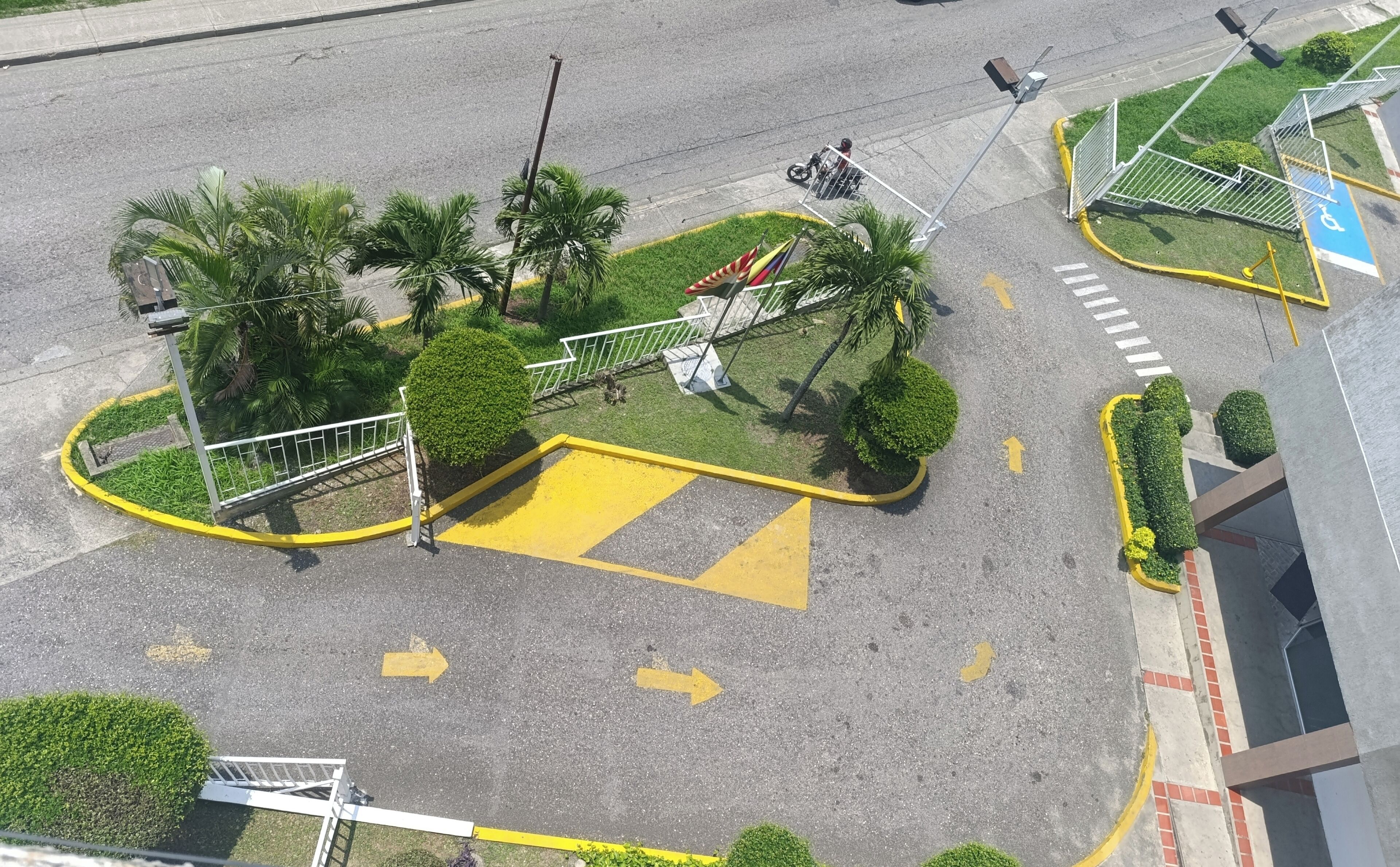An aerial view of a roundabout with palm trees, a pedestrian crossing, and directional arrows on the road.