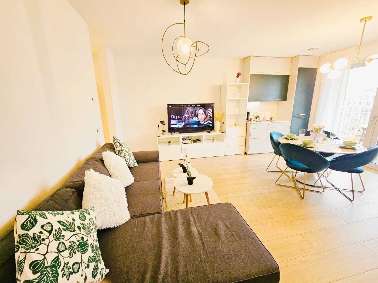 A modern living room with a sofa, a dining table with chairs, a TV, and a kitchen area.