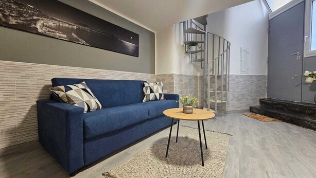 Un salon moderne avec un canapé bleu, une table basse ronde en bois et un escalier en colimaçon.