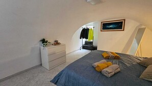 Une chambre à coucher avec un lit, une commode, une plante et un porte-manteau avec des vêtements.