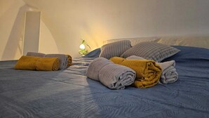 A bed with rolled towels and pillows, a bedside lamp, and a wall-mounted mirror. - In the beating heart of the city-historical center (Napoli)