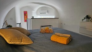 A bedroom with a bed, pillows, towels, a radiator, a plant, and a window. - In the beating heart of the city-historical center (Napoli)
