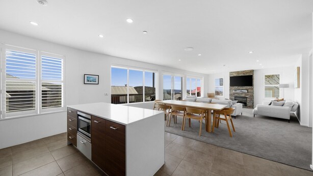 Una cocina moderna con una isla central, comedor con mesa y sillas, sala de estar con sofá y chimenea de piedra.