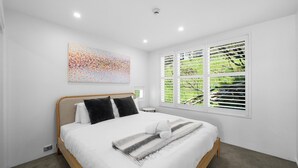 Un dormitorio moderno con una cama grande, una ventana con persianas y un cuadro abstracto de colores en la pared.