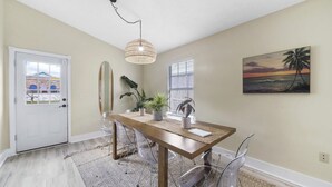 Een eetgedeelte met een houten tafel, transparante stoelen, een geweven vloerkleed en een hanglamp.