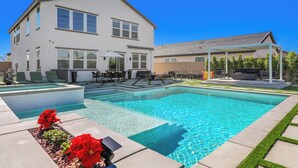 Ein modernes, zweistöckiges Haus mit Swimmingpool, Sitzgelegenheiten im Freien und einer überdachten Terrasse.