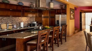 A kitchen with a central island, wooden chairs, a refrigerator, and a tiled backsplash. -  Penthouse suite with dipping pool, palapa & private sunroof overlooking the Bay (Puerto Vallarta)