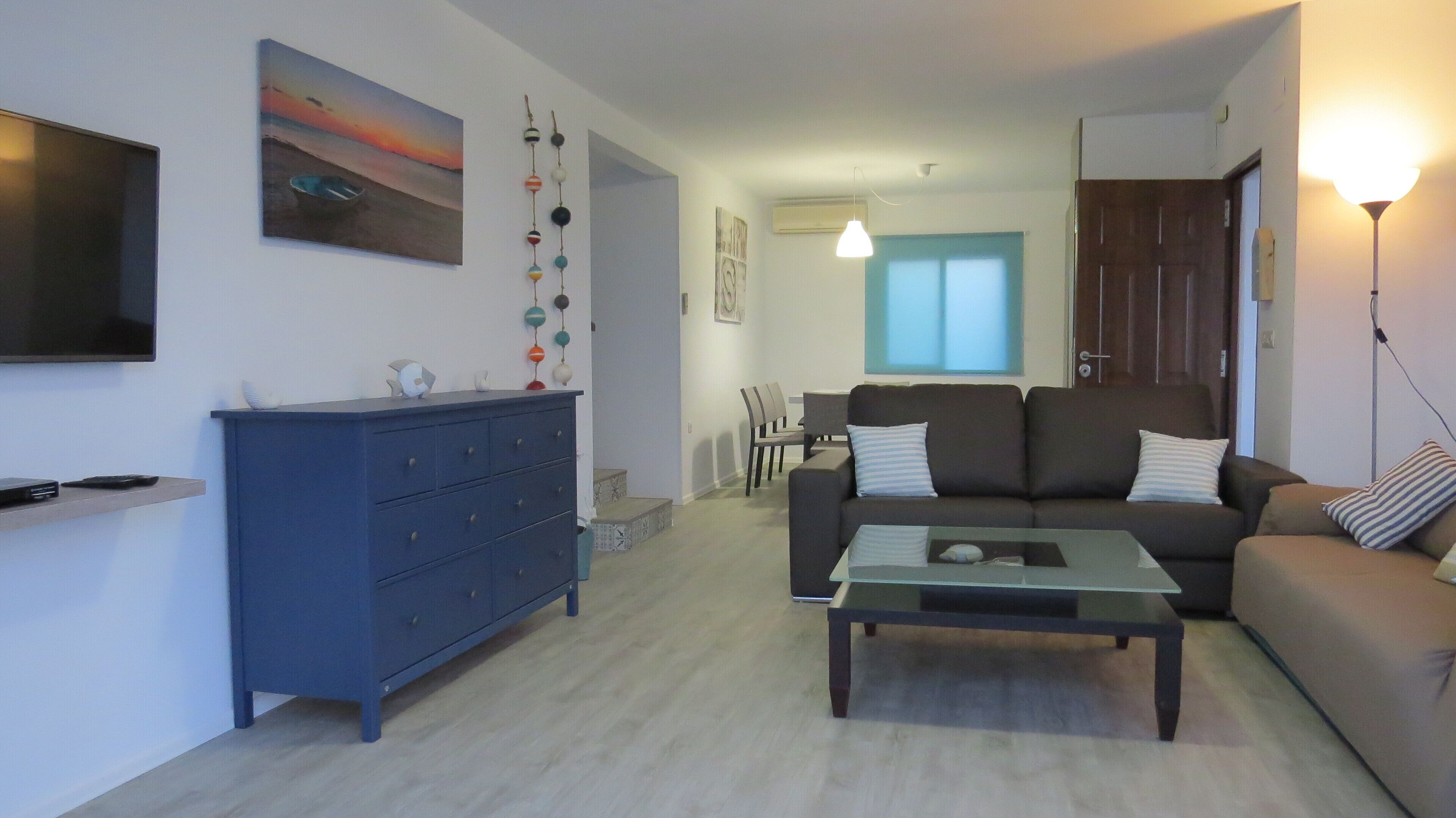 A living room with a sofa, coffee table, and a blue cabinet. There is a painting on the wall and a window with blinds.