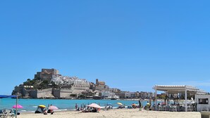 Een strand met parasols, stoelen en een kasteel op de achtergrond.
