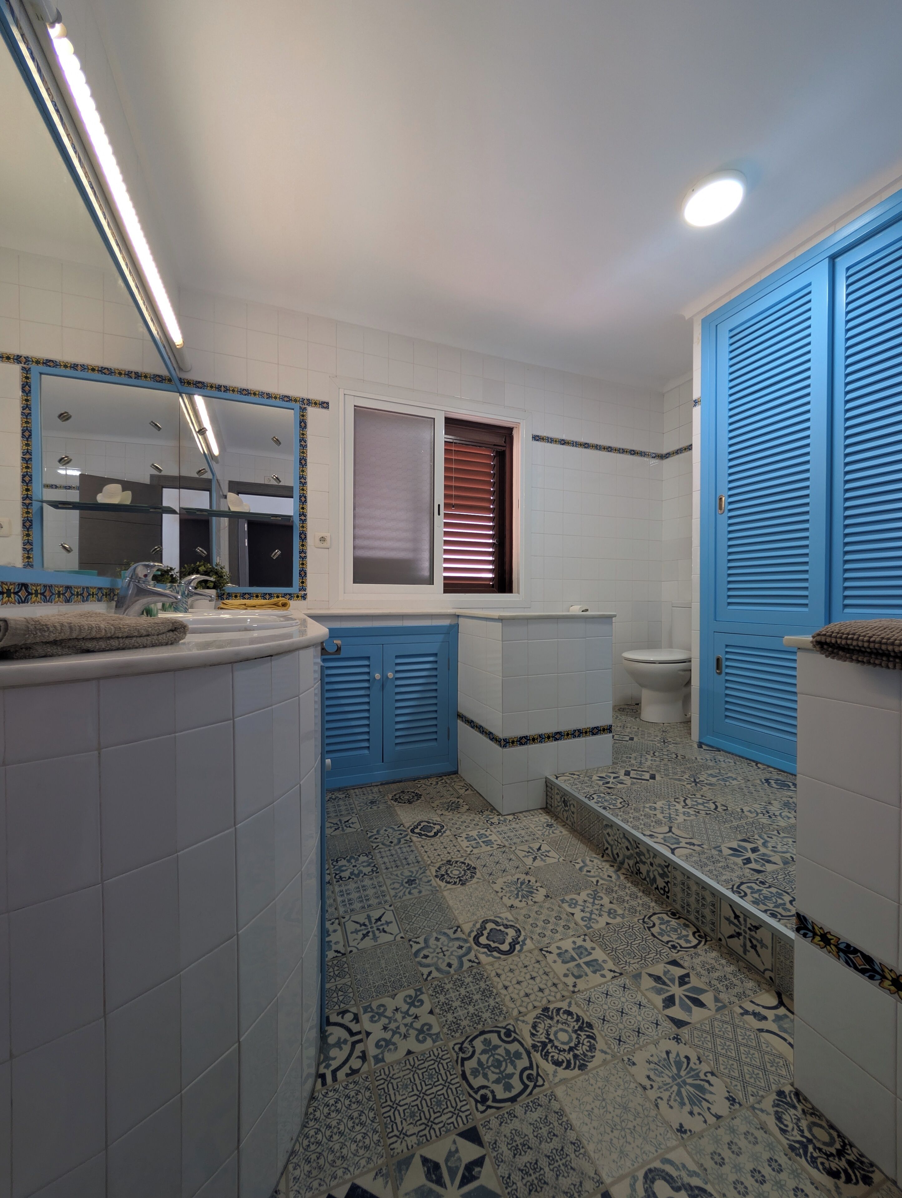 Ein Badezimmer mit Fliesenboden, einem Spiegel, einer Toilette und blauen Schränken.