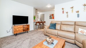 Una sala de estar moderna con un televisor de pantalla plana, mueble de entretenimiento de madera, sofá de cuero color beige y una mesa de centro con objetos decorativos.
