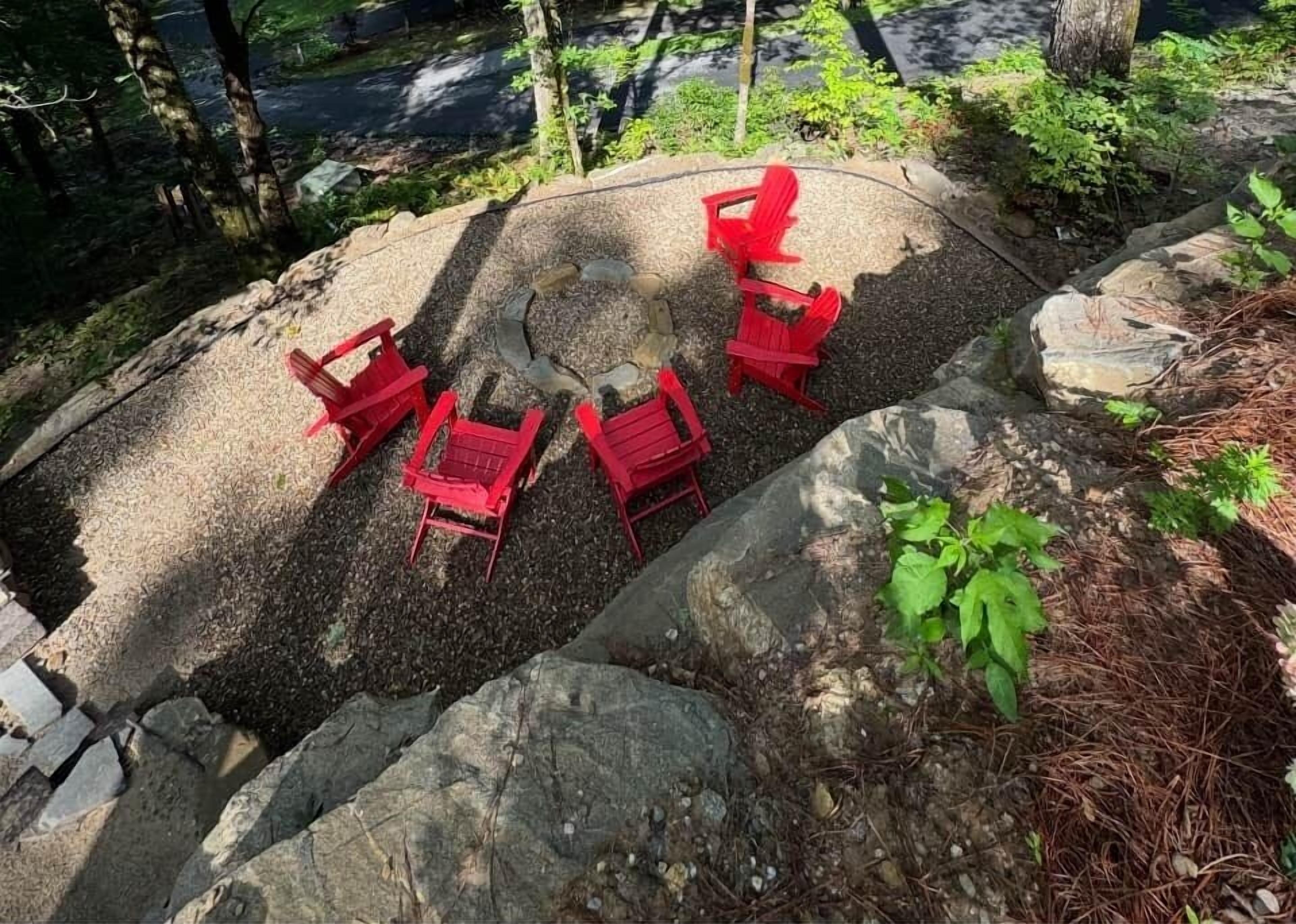 A seating area with red chairs arranged around a stone table, surrounded by rocks and greenery.