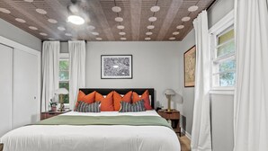Ein ordentlich eingerichtetes Schlafzimmer mit einem großen Bett, einem gerahmten Stadtbild und einer Decke mit runden Leuchten.