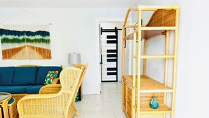 Ein Zimmer mit einem blauen Sofa, Korbstühlen, einem Rattanschränkchen und einer Tür mit schwarz-weiß gestreiftem Muster.