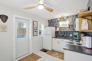 A compact kitchen with white cabinets, a stove, a refrigerator, and a ceiling fan.