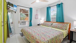 Ein Schlafzimmer mit einem Bett, einem Deckenventilator, einem Fenster mit Vorhängen, einem an der Wand montierten Fernseher und einer Gitarrendeko.