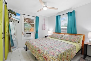 A bedroom with a bed, a ceiling fan, a window with curtains, a wall-mounted TV, and a guitar decoration.