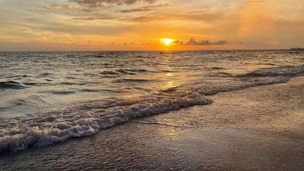 Ein Strandbild mit Wellen bei Sonnenuntergang.