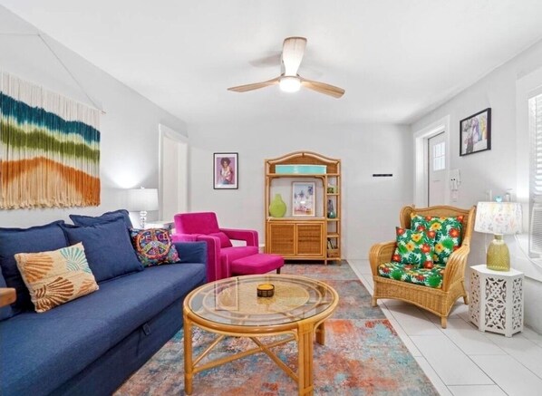 A living room with a sofa, a coffee table, a chair, a bookshelf, and a ceiling fan.