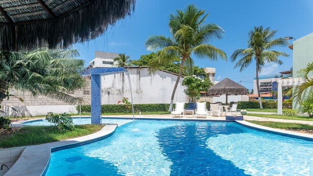 A swimming pool with a blue mosaic border, surrounded by palm trees and lounge chairs.