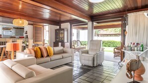 A spacious living area with a sofa, armchairs, and a dining table. A kitchen with a microwave and cabinets is visible in the background.