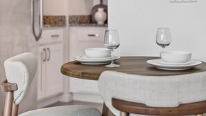 Un comedor con una mesa redonda de madera dispuesta para dos personas, platos blancos y copas de vino.