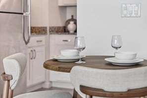 Un comedor con una mesa redonda de madera dispuesta para dos personas, platos blancos y copas de vino.
