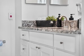 A bathroom with a marble countertop, a black wicker basket, a plant, a black soap dispenser, and a faucet. - Luxury Spot / Game room / Pool / Cinema / Spa / Downtown access (Fort Myers)