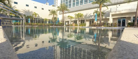 A swimming pool with clear water, surrounded by palm trees and a modern building with large windows.