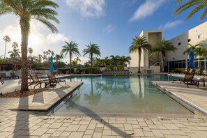 A pool area with palm trees, lounge chairs, and a modern building in the background.