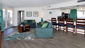 A living room with a sofa, coffee table, and chairs, a kitchen area with a dining set, and a view through a sliding door. - Relax in Style: 2BR Ocean View Condo at Atlantic Terrace (Daytona Beach)