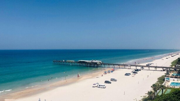 A beach with a pier extending into the ocean, a sandy shore, and a clear blue sky. - Relax in Style: 2BR Ocean View Condo at Atlantic Terrace (Daytona Beach)